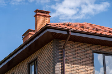Obraz premium Corner of house with new brown metal tile roof and rain gutter. Metallic Guttering System, Guttering and Drainage Pipe Exterior