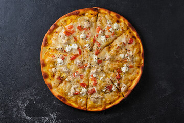 Pizza with tomatoes, chicken, onions, feta cheese, mozzarella cheese and spices. Flat lay. On a dark background.