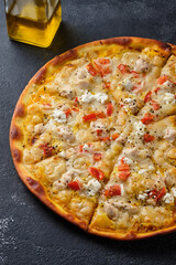 Pizza with tomatoes, chicken, onions, feta cheese, mozzarella cheese and spices. On a dark background.