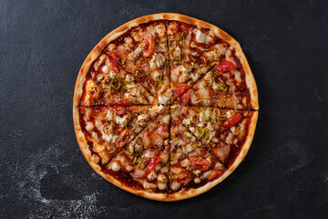 Pizza with tomato, chicken, ham, onion, sesame, mozzarella cheese, spices, tomato sauce and teriyaki sauce. Flat lay. On a dark background.