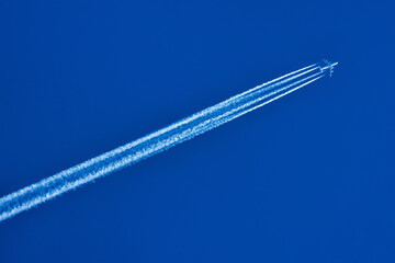 A jet flying high in the blue sky with a white trace behind.