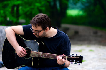 Young man wearing glasses playing guitar sitting on the old Roman bridge