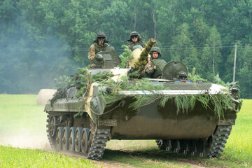 infantry combat vehicle rides on a dirt road along a field against the background of a forest with...