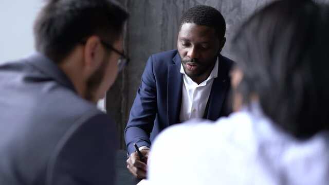 Handsome african american businessman talking in negotiations with asian partners sitting at the table