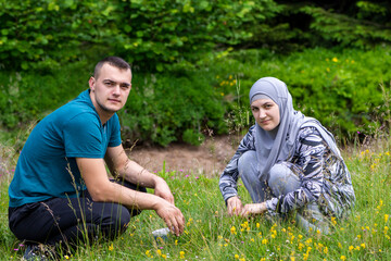 Young muslim couple squatting on grass and looking to the camera with different face expressions. Love, lifestyle and nature concept