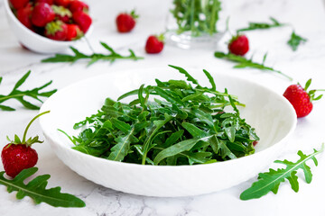 Summer salad of strawberry with arugula, spinach leaves in white plate on marble table with salad...