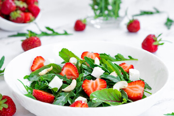 Vegan salad of strawberry with arugula, spinach leaves, feta cheese and cashew nuts with salad leaves and fresh strawberry fruits around. Healthy ogranic food, vitamins and antioxidants.