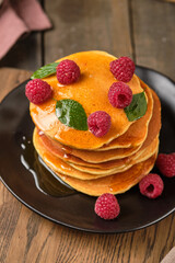 Flavored pancakes with honey and fresh raspberries for breakfast. Great breakfast dessert, garnished with fresh mint leaves.