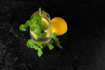 A large glass of water with lemon, mint leaves and ice, covered with water droplets.