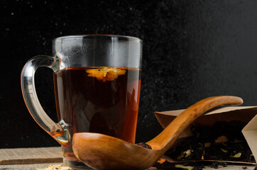 A glass mug of fragrant brewed flower tea on a wooden table, with a wooden spoon