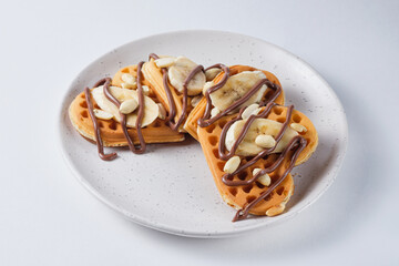 Sweet Belgian waffles for breakfast on a white plate. Waffles with peanuts, banana and chocolate spread.