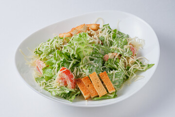 Fresh salad with iceberg lettuce, tomatoes, chicken, cheese, garnished with croutons. Salad in a plate on a white background.