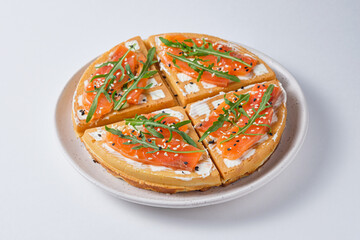 Salted Belgian waffles for breakfast on a white plate. Waffles with salmon, cream cheese, arugula and sesame seeds.