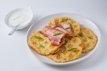 Hearty potato pancakes with bacon and sour cream, garnished with fresh green onions. Dish on a white plate.