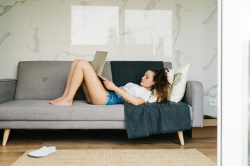 beautiful young woman sitting in laying in couch working remotely