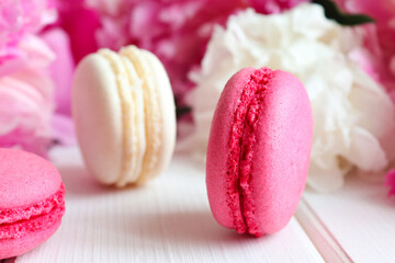Cozy bakery and floral background. Close-up macarons and peonies on a white wooden table. Selective focus