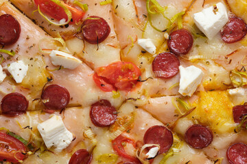 Pizza with tomatoes, ham, onions, feta cheese, mozzarella cheese, spicy sausages, spices and mustard sauce. A closeup of a pizza.