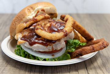 Barbeque chicken sandwich stacked tall in the toasted bun with huge onion rings on the side to fill the entire plate