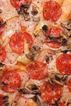 Pizza with tomatoes, ham, spicy kalbasa, mushrooms, mozzarella cheese, spices and tomato sauce. A closeup of a pizza.