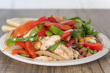 Chicken fajitas, hot off the grill piled high with vegetables and large chunks of meat on a plate with tortillas