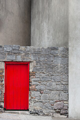gray concrete facade with a volcanic stone wall and a red wooden door in waterford, Ireland