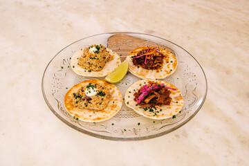 Four tacos of two flavors. Chicken tinga and cochinita pibil on a glass plate