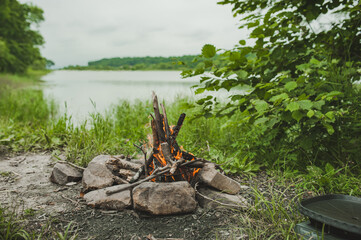burning fire with wood and bright orange flame in green summer forest near lake, summer sea camping, travel content