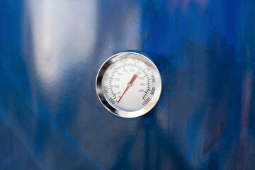 Circular Temperature gauge thermometer for measuring hot and steam temperature mounted on blue metal. Industrial concept