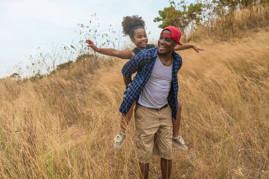 african american father and daughter ridding piggyback on mountain