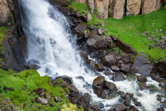 Closeup of the bottom of rocky waterfall with vibrant green vegetation growing round large boulders and white water.