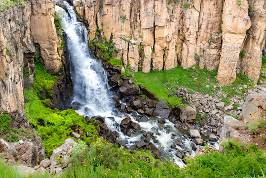 Waterfall in the wilderness with stunning rock cliffs and vibrant vegetation below.