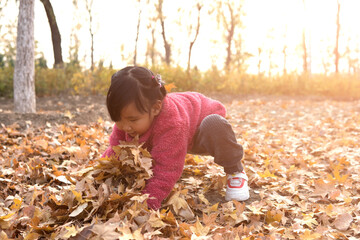 Child outdoors hugs fallen leaves on the ground