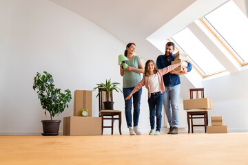 Portrait of happy caucasian family moving in new apartment with cute little girl carrying boxes and belongings.