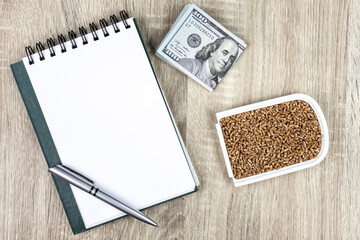 Top view mockup of open blank notebook on spiral, automatic pen. 100 dollar banknotes and samples wheat seeds, conceptualizing agricultural commodities. on a wooden table
