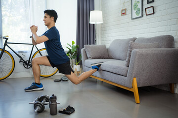 Fototapeta premium Active young man watching online training video on laptop. He's stretching during his morning workout at home.