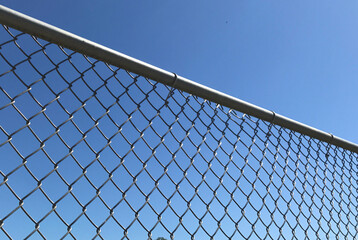 Closeup of a metal chain link fence with a clear blue sky background