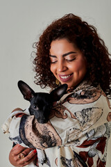 Obraz premium MUJER LATINA SONRIENDO MIRANDO SU MASCOTA EN BRAZOS UN FONDO BLANCO