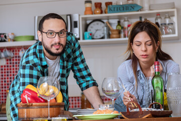 Pareja de jóvenes tienen un momento de relax en la cocina mientras preparan la cena para disfrutar...
