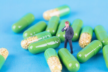 Miniature figures of business men standing among a pile of capsule medicines