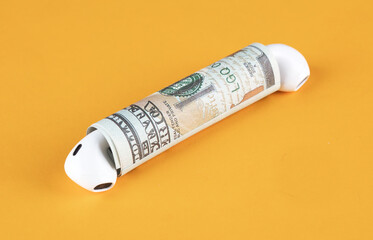 A bluetooth headset is placed on each end of the rolled dollar bill