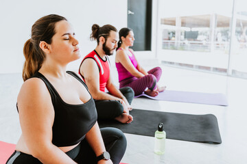 Plus size young hispanic woman sitting while practicing meditation during yoga session in Latin America