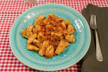 45 degree view of plate of gnocchi with tomato sauce served in a light blue vintage plate on a table with red and white tablecloth