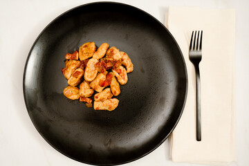 Black plate of Gnocchi with red sauce on a white marble table. Accompanies a modern black fork.