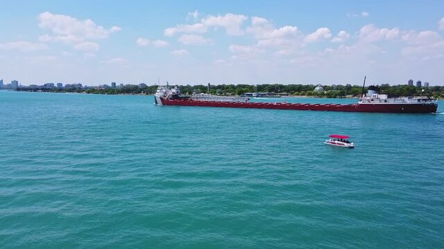 Large ship cruises past pontoon boat down the Detroit River
