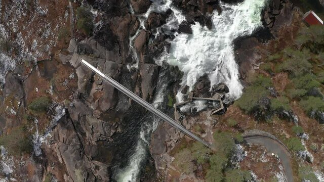 An aerial view of the Likholefossen waterfall in Gaular, Norway. Raging whitewater whirling and splashing, fed by the melting snow in the mountains. A still bridge crossing the river.