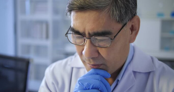 Asian man doctor scientist thinking, confused about an idea, would be trying to find a solution in laboratory tube testing blue liquid. Medical science health care concept.