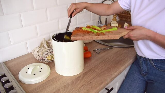 Adult woman puts cleaning of vegetables into compost bucket. People veggie. Home kitchen interior. Zero waste concept.