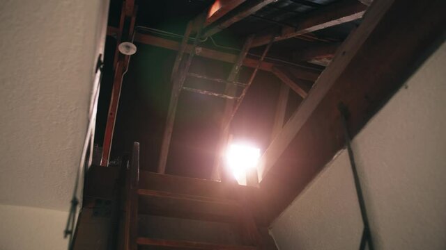 Bottom View of an open vintage roof hatch, seeing the skylight with a sunny lens flare and the timber beams of an old farmhouse