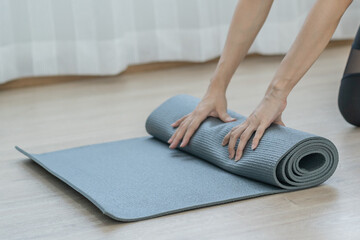 Workout, hobby asian young woman folding, rolling gray rubber carpet, fitness mat to keep after yoga session finished,  training in class, room at home. Healthy fitness exercise, sport for wellbeing