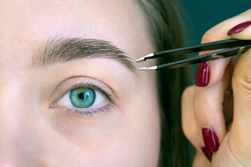 Beautiful girl with eyelashes tweezing her eyebrows in a beauty salon. Woman doing eyebrow...